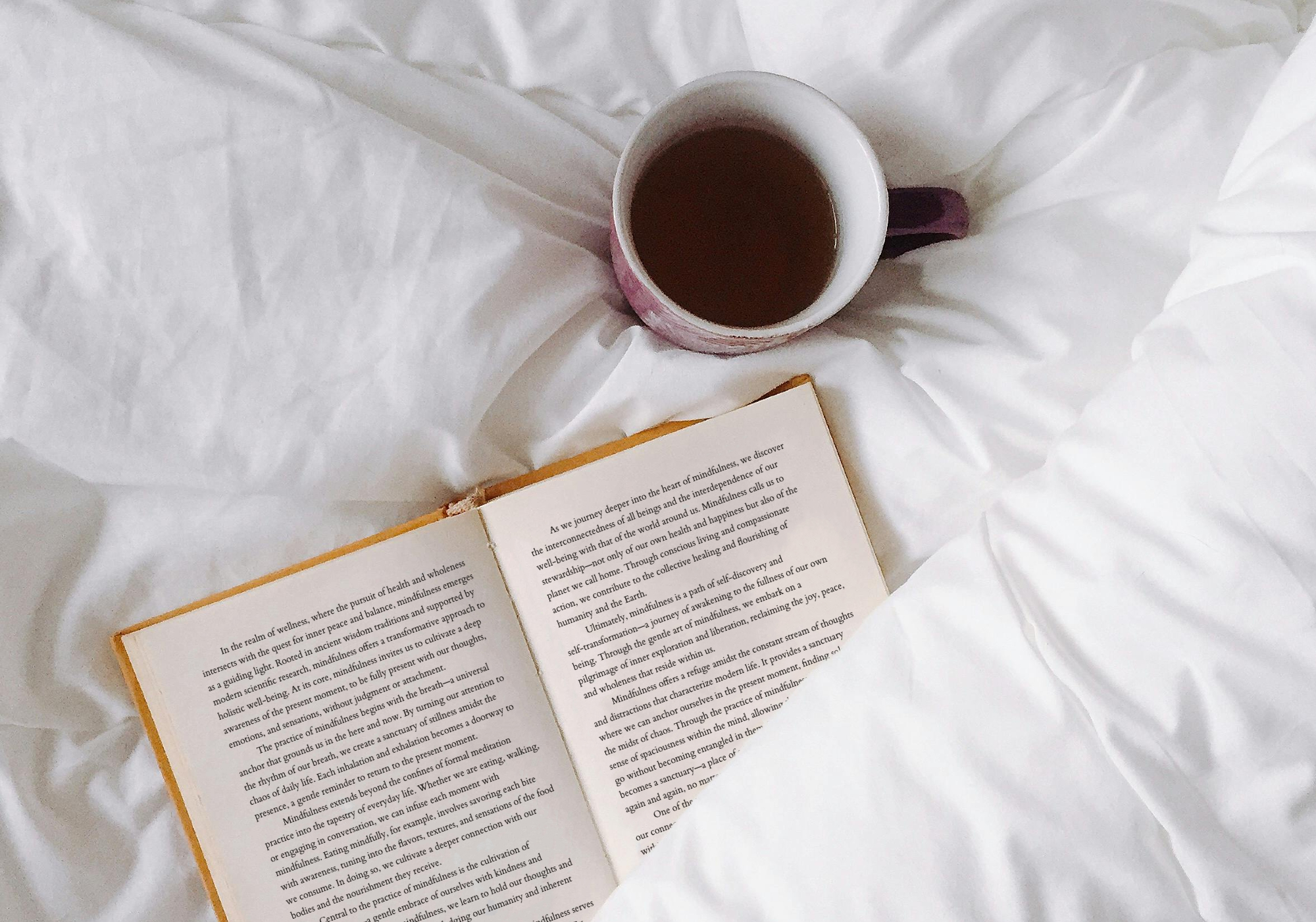 Cup of tea and open book on bed.