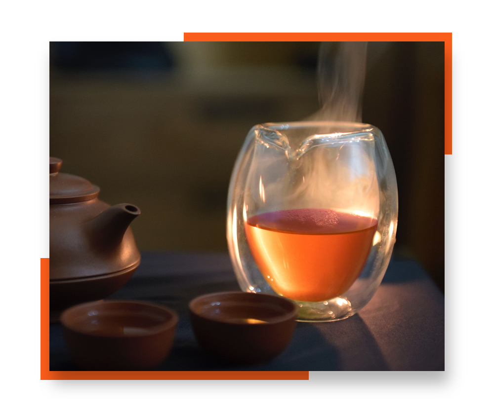 A glass of black tea, with a clay teapot and teacups pictured as well. The image is bordered by orange accent colors.