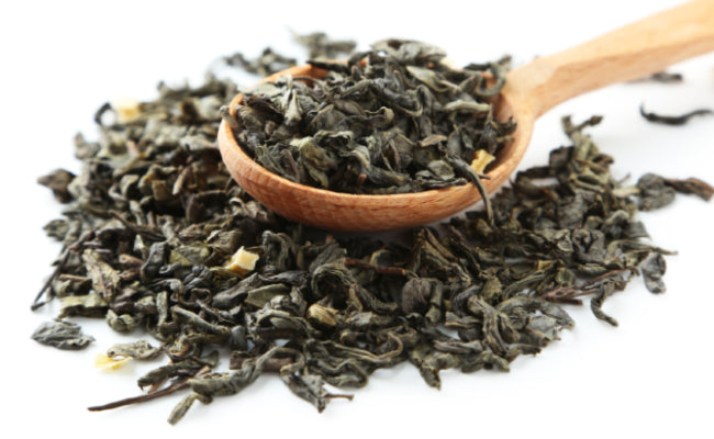 A wooden spoon, full of loose leaf tea, resting on a small pile of the same loose leaf tea.