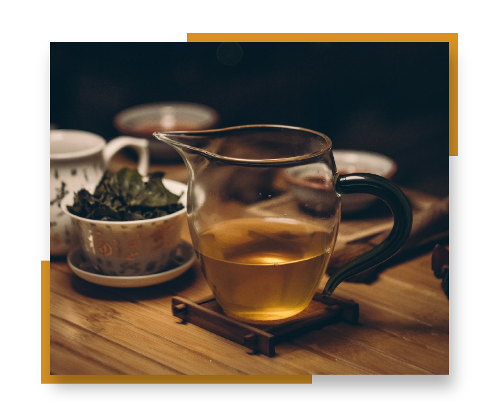 A golden cup of oolong tea sitting on a tray, surrounded by other tea cups. Image is bordered by golden accent colors.