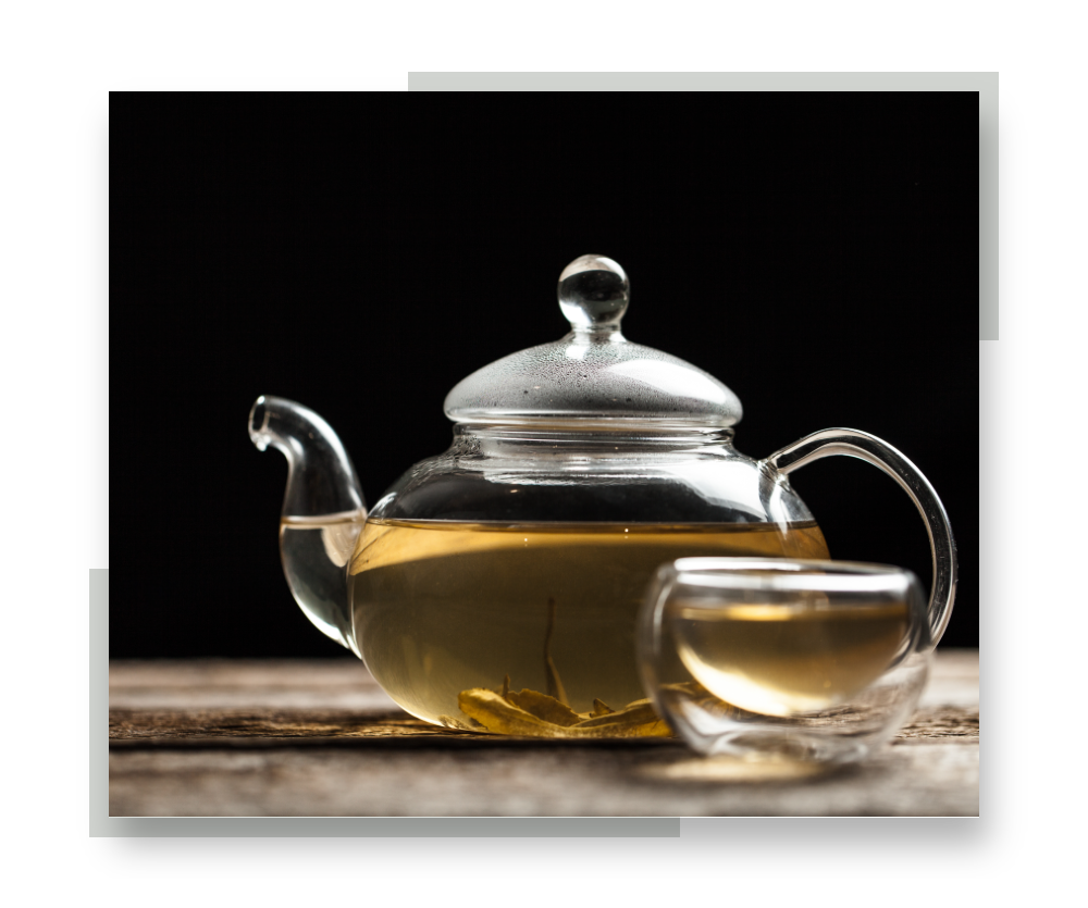 A glass teapot of white tea with a glass teacup in front of it. The image is bordered by silver accent colors.